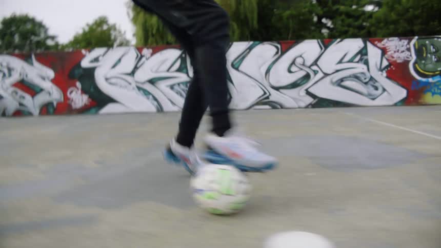 A teenage boy is practicing his soccer skills on pavement in a park