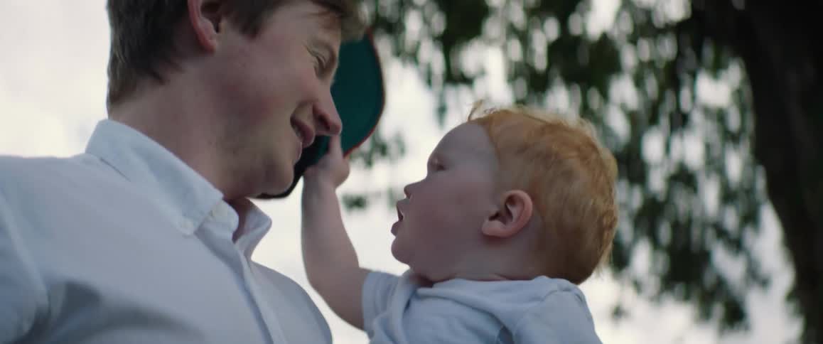 A baby takes a baseball cap off of his head and places it on the head of the man carrying him