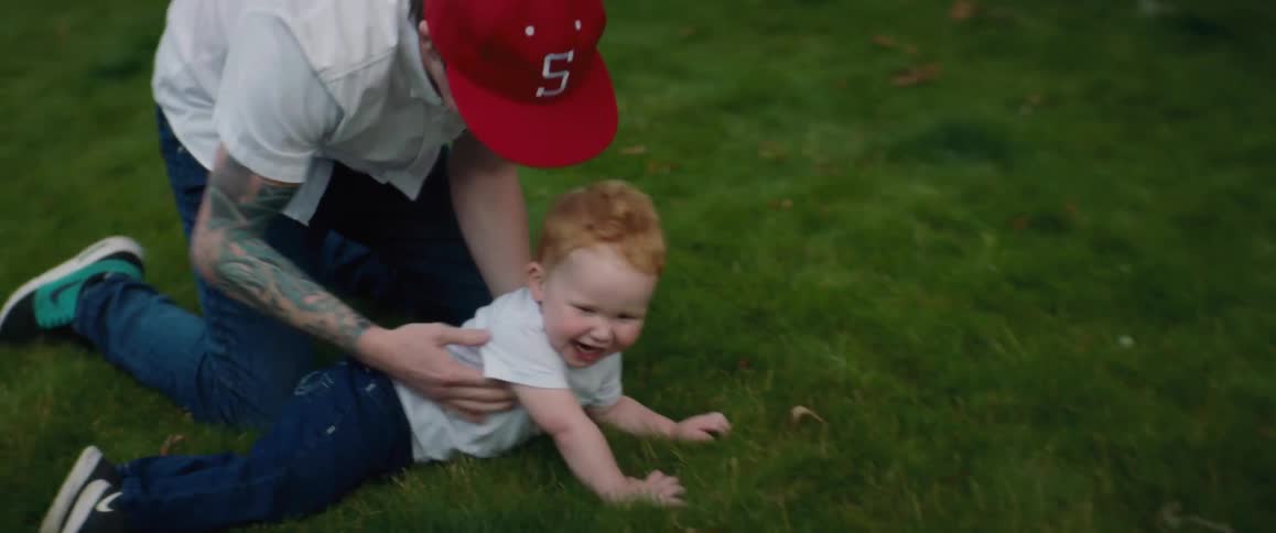 A little boy laughs as his dad chases him in the yard catching him and tickling him in the grass