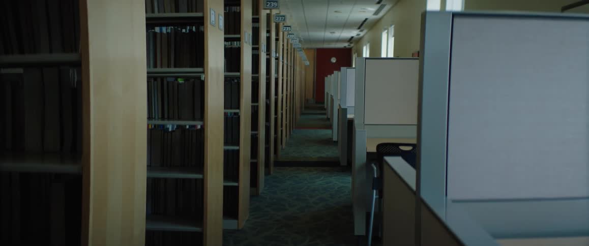 An empty library has rows of book shelves and a long line of cubicles