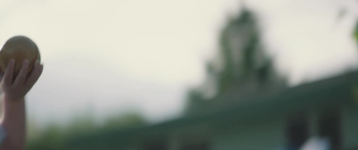 A small boy is outside smiling and laughing and he takes a ball from his father and throws it then runs and picks it up