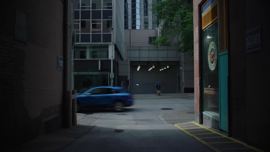 A car drives past an alley in a city as people walk down the street