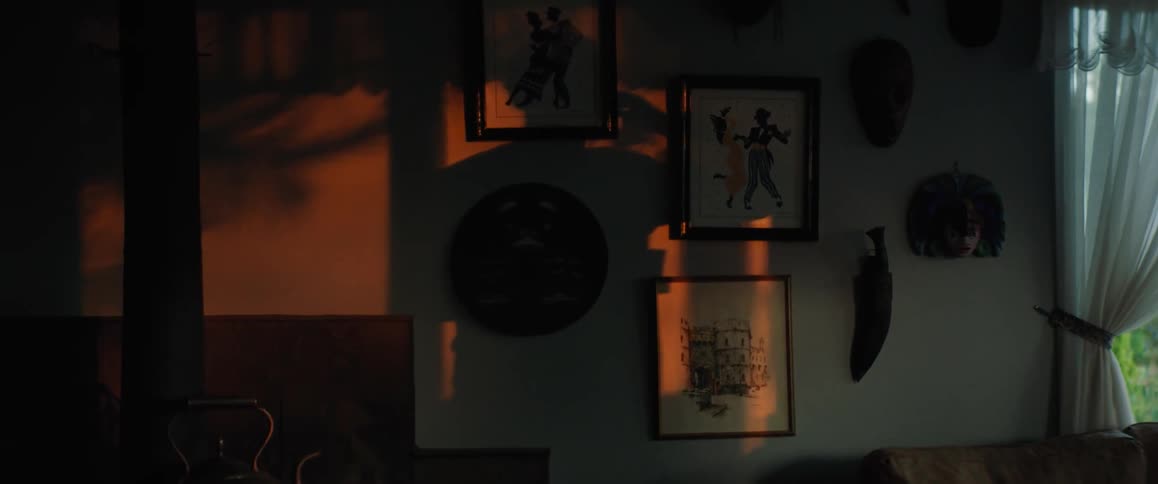 A mans shadow is on the wall as he walks around holding a coffee cup and talks on the phone