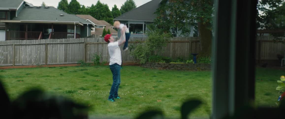 Window shows view of father holding and playing with son in backyard