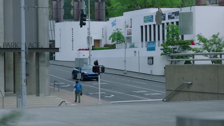Woman in blue shirt walks down the street passing by tall building and highway in the city