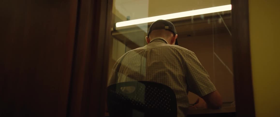The back of a man sitting at a library cubicle desk reading a book