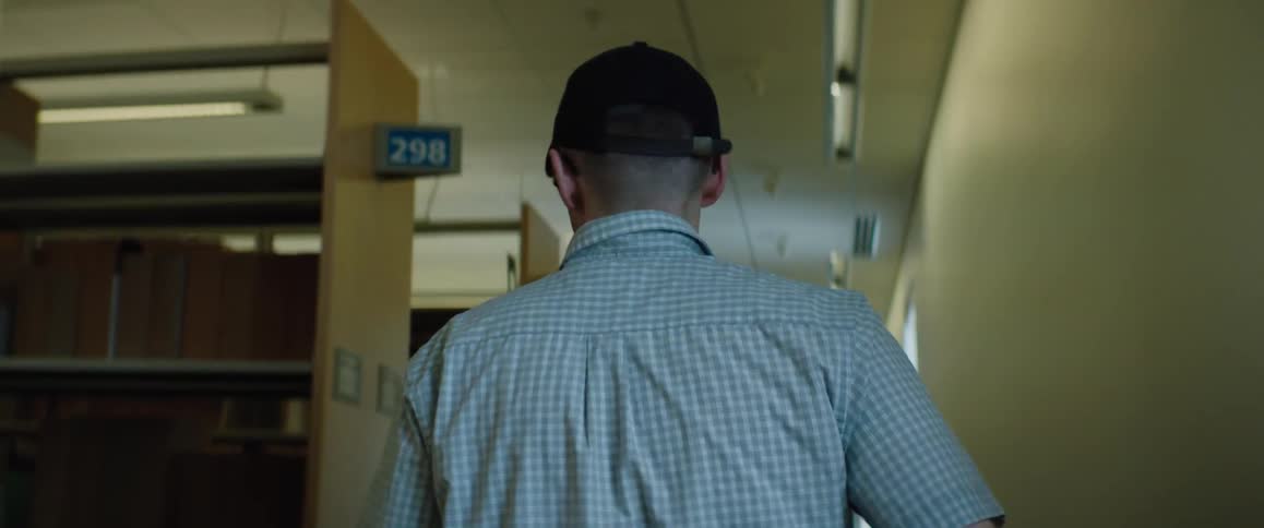 Man with navy blue cap glasses and shirt walks along the hall of large library