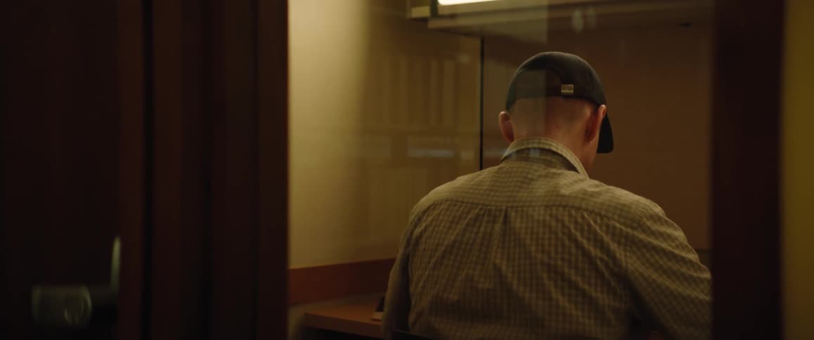 A man wearing a dark cap is standing in a small room with his back turned