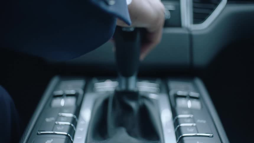 A driver wearing a suit jacket and watch puts his car into gear