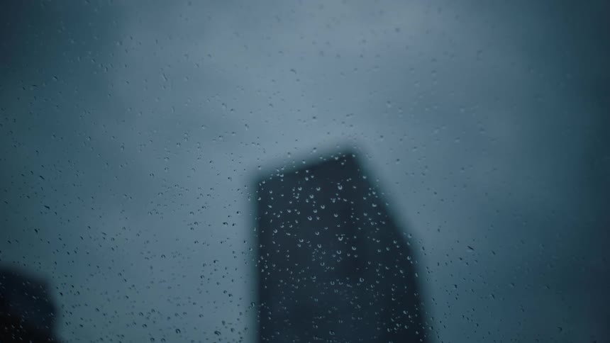 Tall building sillhouette seen from behind car windows on cloudy and rainy day
