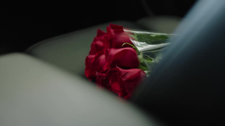 A bouquet of red roses sits in the passenger seat of a traveling car