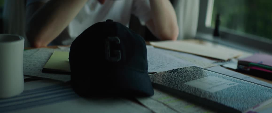 A man is sitting at a table with a hand written letter in front of him and he puts his cap on the table