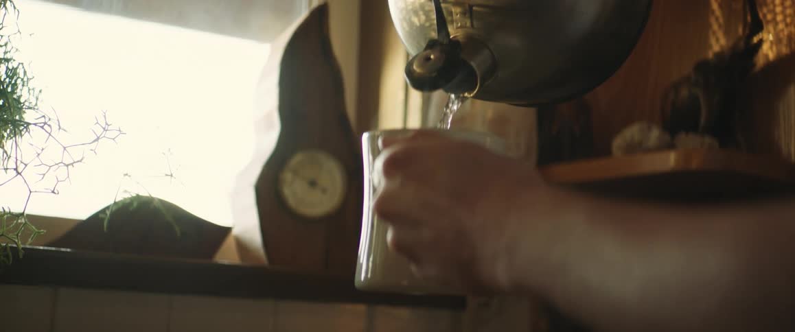 Someone is pouring hot water from a teapot into the cup they are holding