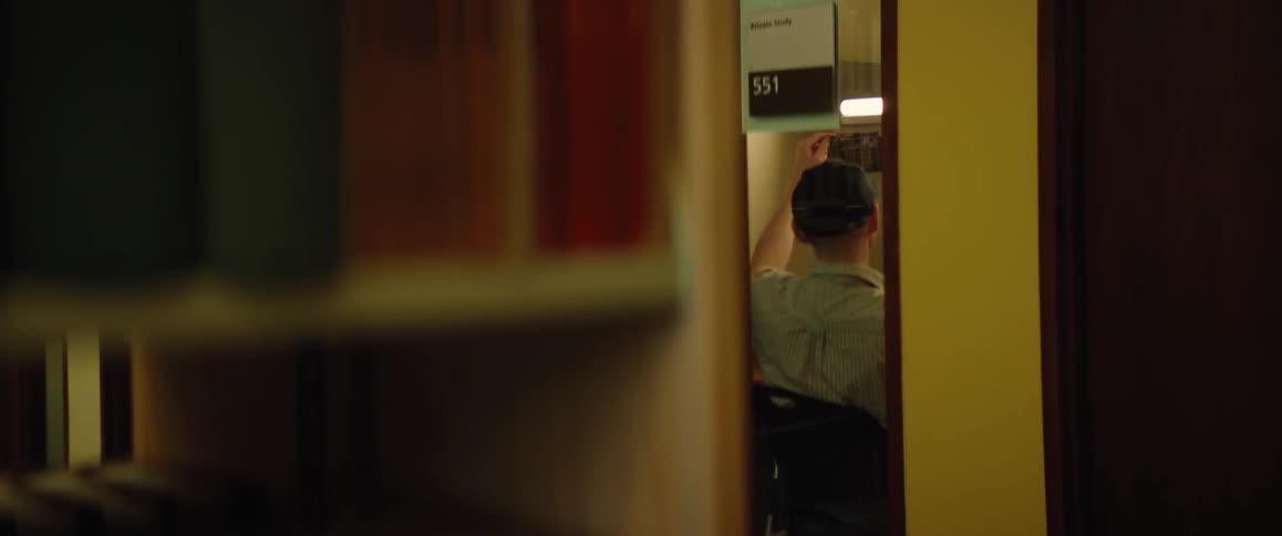 Man sits working under light near bookshelves