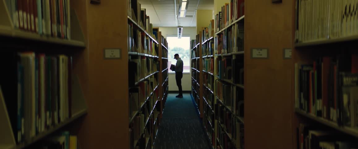 A man takes a book off of a shelf in a narrow aisle of a library