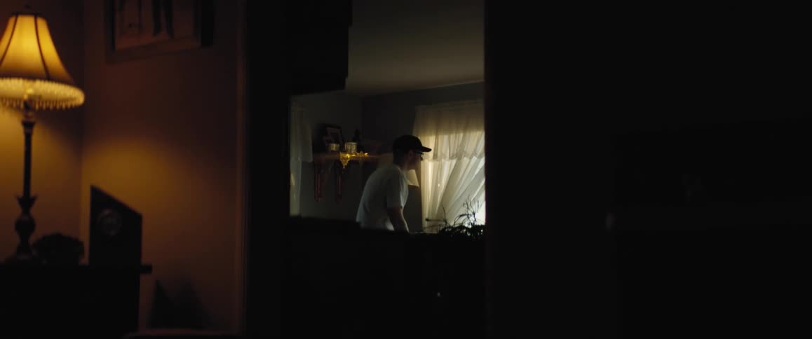 A man walks through his living room and sits down in a chair by the window