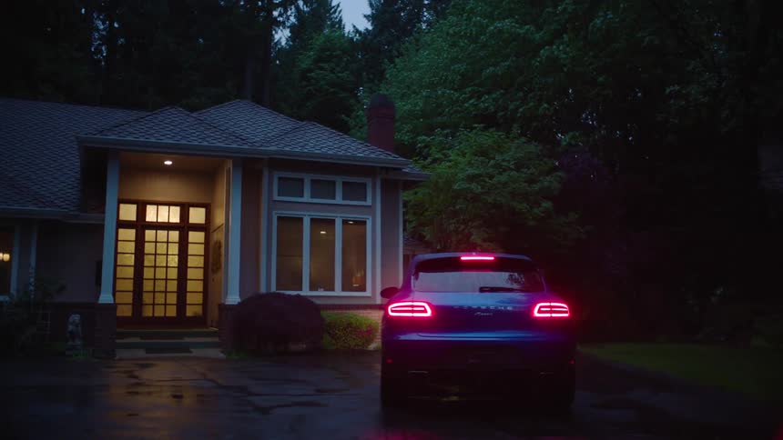A car pulls into a driveway and parks arriving home where lights are on