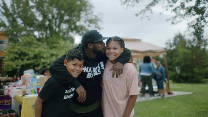 Father hugs and kisses son and daughter while posing at family outdoor picnic in the park