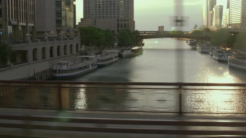 A view crossing a bridge over the Chicago River with the sun shining off the water between buidlings