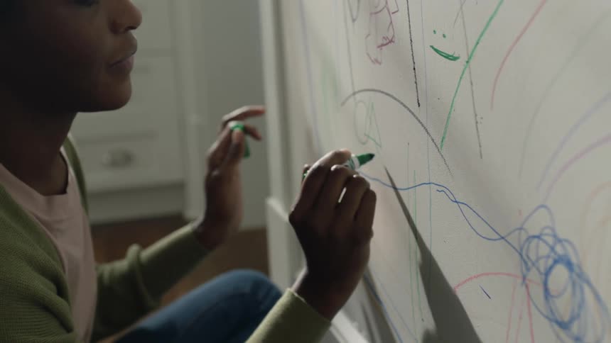 A teenage girl is talking to a child as she draws on the wall with colored marking pens