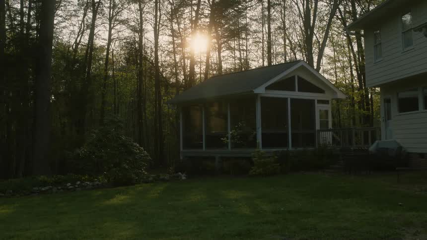 The sun shines through trees over a house in a neighborhood