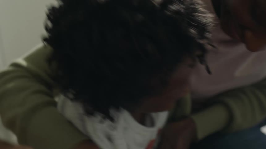 A teenage girl is sitting on the floor with her little sister and they shake hands and hug