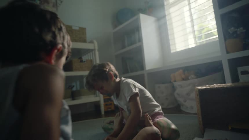 Two little boys are sitting on the floor in a room with toys and one boy is covered in ink and writing on the other boy with marking pens