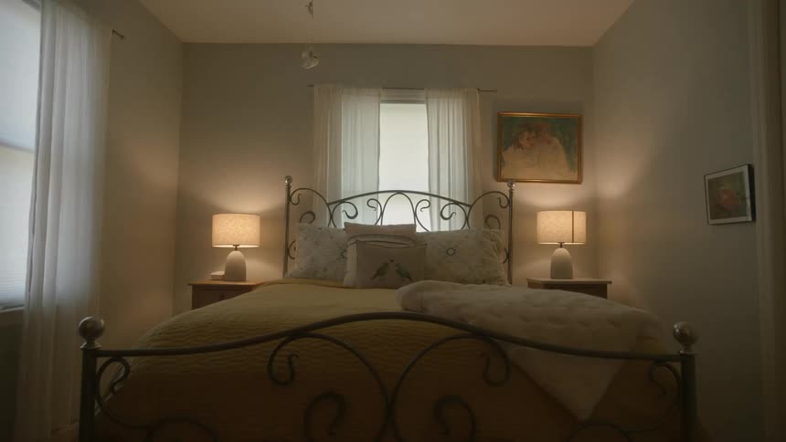 The bed is made in a bedroom and the lamps on the nightstands are left on