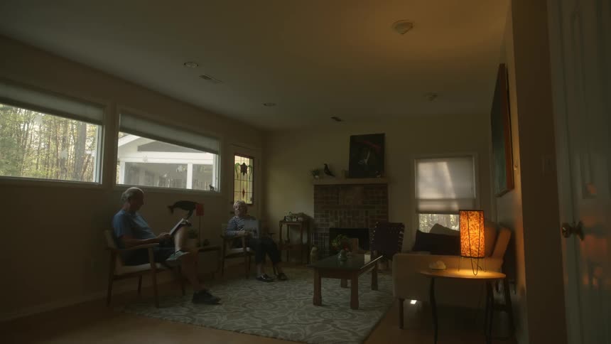 Elderly couple sit in living room reading and talking