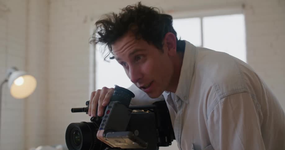 Filmmaker directing actors while filming a scene inside a white room