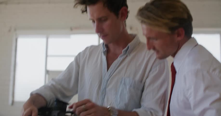 Two men are talking in a room together and looking at camera equipment