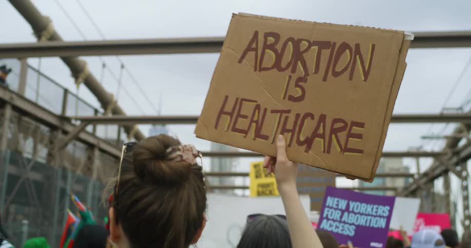 A woman holds a homemade sign into the air while marching across a bridge alongside a crowd of protesters
