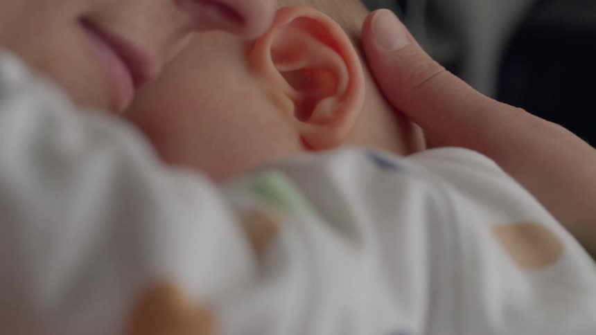 A woman strokes the hair of a baby with her thumb while embracing him