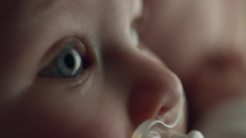 A young baby sucks on its pacifier as it looks attentively into the distance