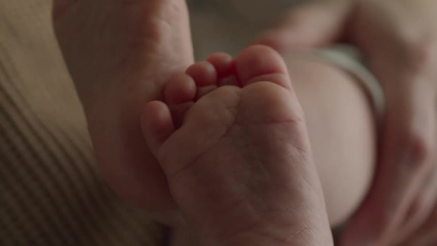 A baby moves their feet as an adult holds their leg