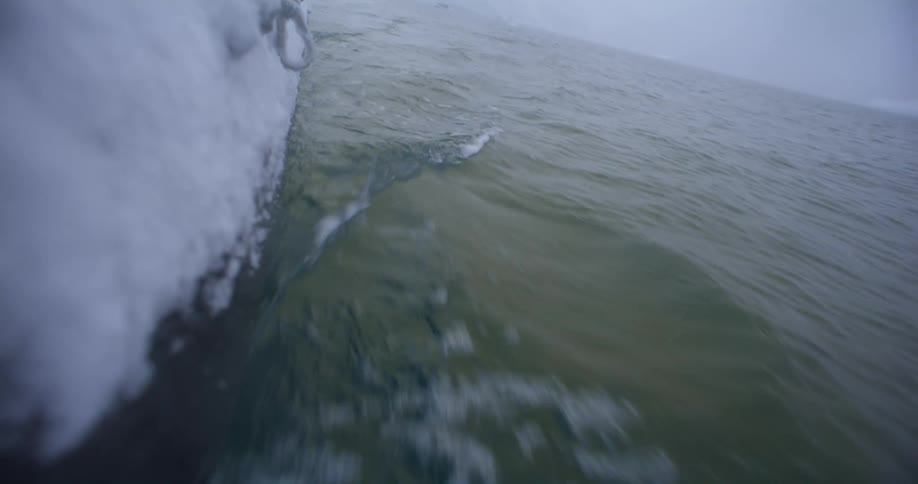 The ice and snow covered side of a boat as it travels through water on a gray day