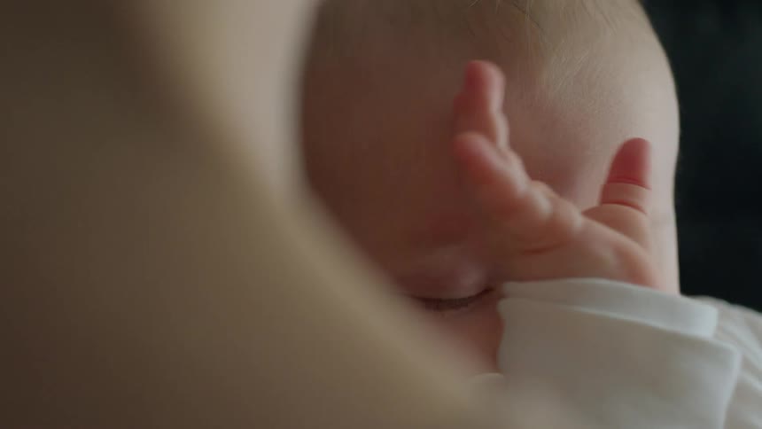 A baby with a pacifier in their mouth is rubbing their head with their hand