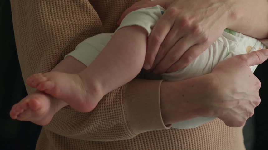 A mother holds her newborn baby in her arms and rubs its bottom