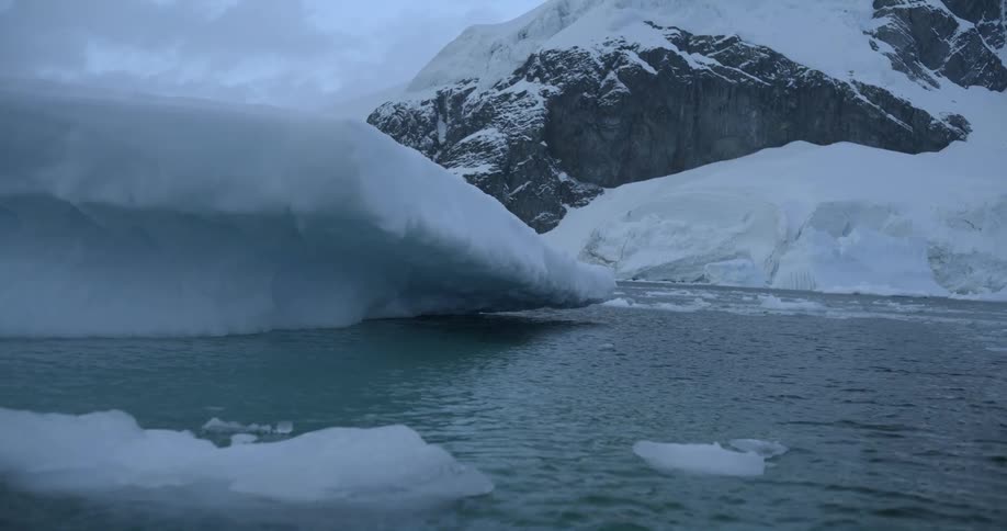 Large pieces of ice float across the water and there is a snow covered mountain in the distance