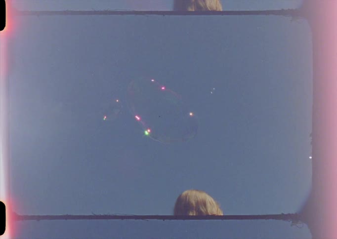 A young woman long blond hair is outside making large bubbles and they shine in the sunlight