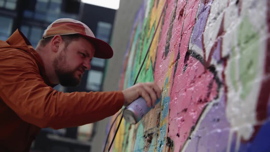 A man paints a mural on a wall in a neighborhood