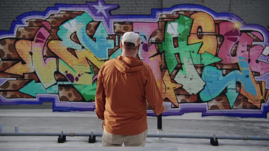 A man stands in front of a mural he painted on a building