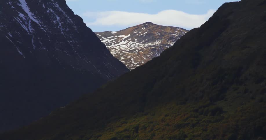 Snow on a mountain can be seen between two mountains and the peak is high in a cloudy sky