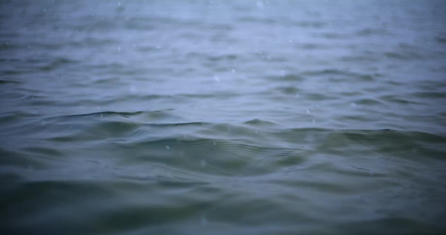 Sunlight reflects on the water as it waves and ripples and snow falls from the sky