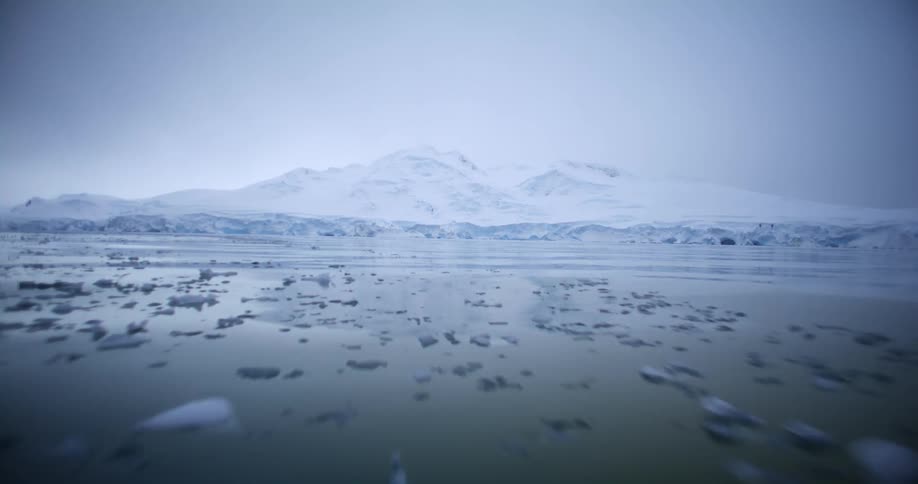 Chunks of ice and snow fill the ocean below a snow covered mountain