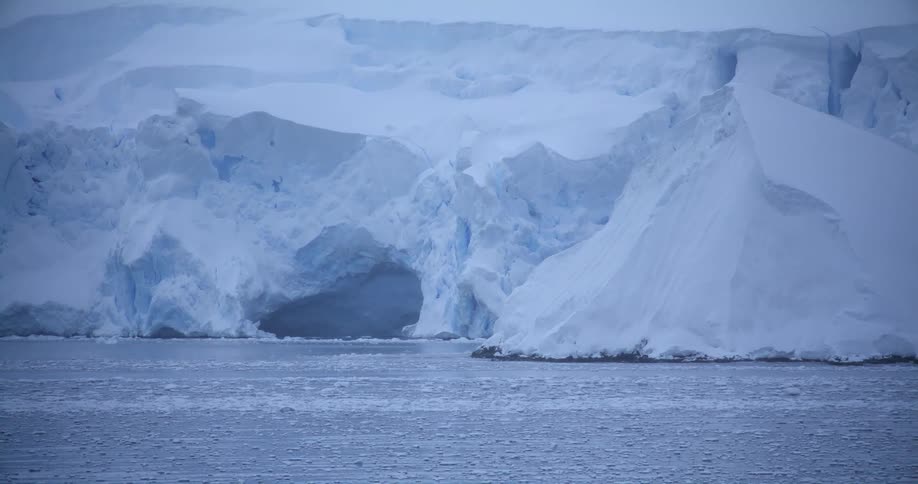 Pieces of ice are moving in the water past a huge snow covered iceberg