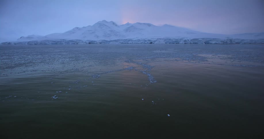 Light reflects on the rippling water as pieces of ice are floating near a snow covered mountain