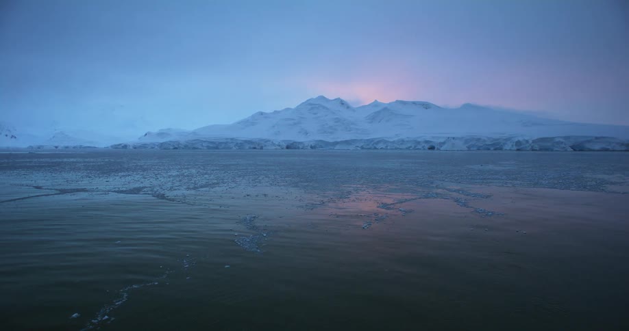 Sunlight is behind a distant frozen mountain in the arctic
