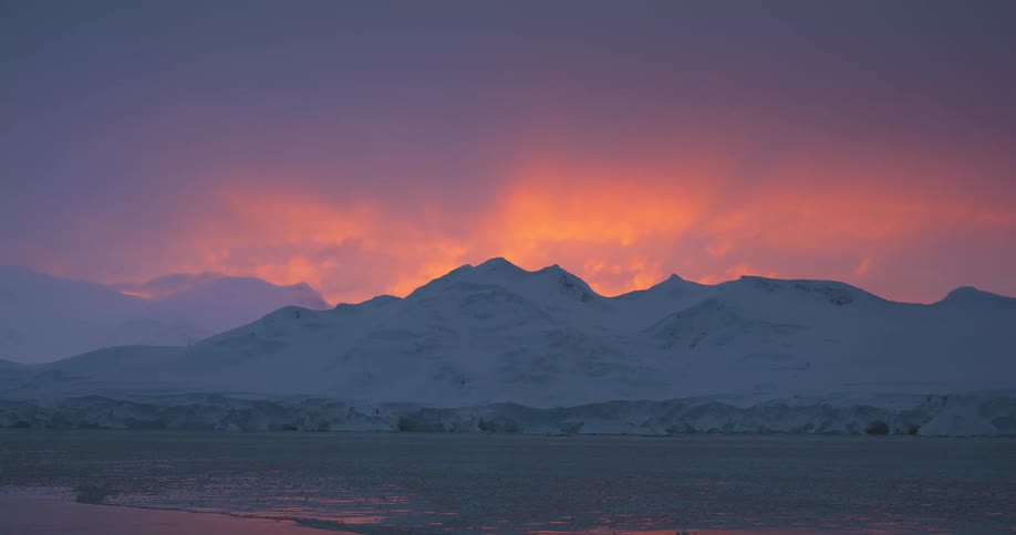Sunset behind the snow covered peaks of artic mountains near the ocean