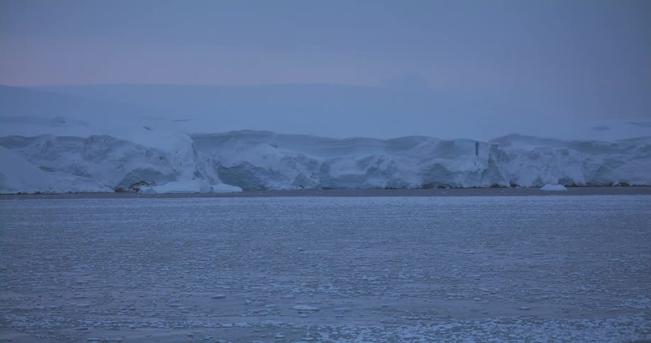 Pieces of ice are floating in the water in front of a snow covered mountain